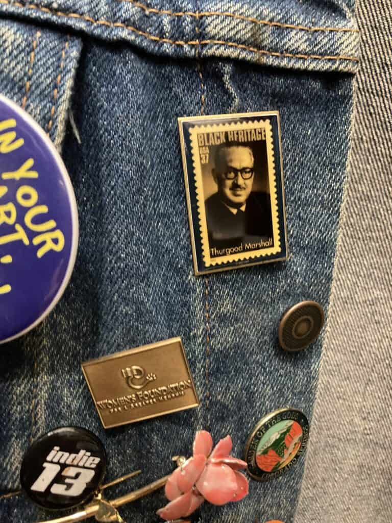 A photo of my jean jacket with lapel pins, one of which honors the work of Thurgood Marshall. 