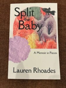 A photo of the cover of the memoir "Split the Baby" by Lauren Rhoades featuring a white background and a multicolored image with a black fish in the top right corner. 
