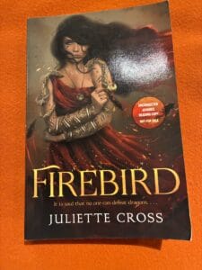 Cover of Firebird featuring a dark-haired women in a dramatic red dress with gold bracelets forming snakes and flickers of flame. 