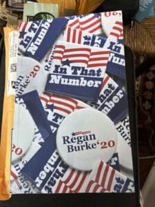 Red, white and blue book cover with the name of the book "In that Number" rendered as a refrigerator magnet and author name "Regan Burke '20" as a campaign button. The story is what happens when we write into the marrow.