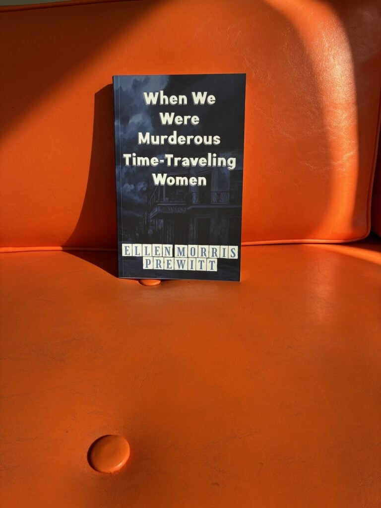 When We Were Murderous Time-Traveling Women in a dark blue cover propped on an orange couch, one couch button showing.